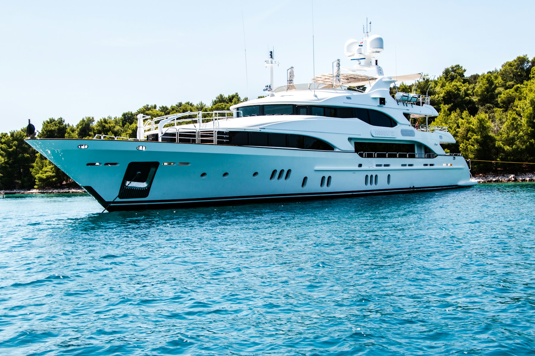 Superyacht moored in turquoise water beside a wooded shoreline