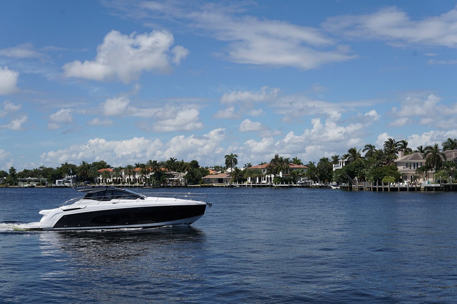 A motor yacht cruising the Intracoastal Waterway in Fort Lauderdale, with palm trees, waterfront homes and private docks behind it